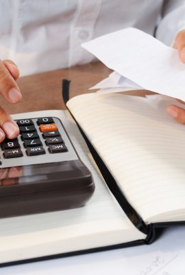 Closeup of person calculating bills on calculator. Notebook and calculator lying on desk. Accountancy concept. Cropped view.